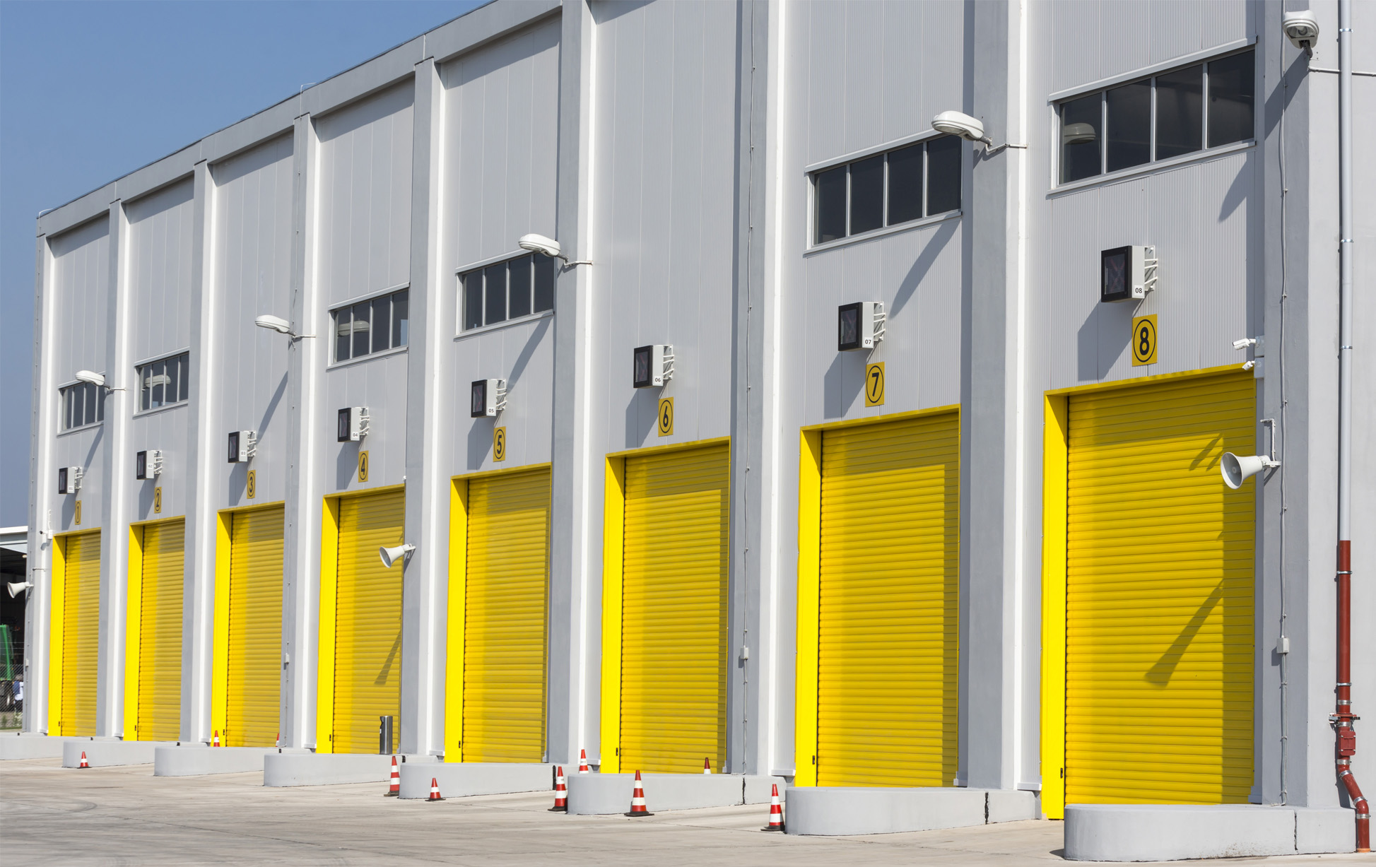 An industrial warehouse with eight large yellow drive-in doors for big trucks.